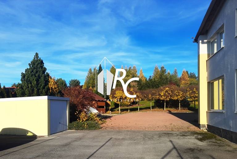 Dvůr rodinného domu v Necpalech s dlážděnou plochou a zeleným pozadím.