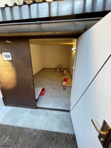 Interiér garáže s otevřenými dveřmi, podlaha s dřevěným dekorem, úložný prostor.