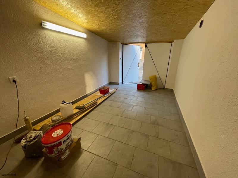 Garáže s nářadím a osvětlením, podlaha s dřevěným dekorem, otevřené dveře na denní světlo.