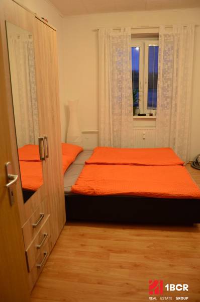 Ložnice v 2-pokojovém bytě s postelí, šatníkem a podlahou s dřevěným dekorem.