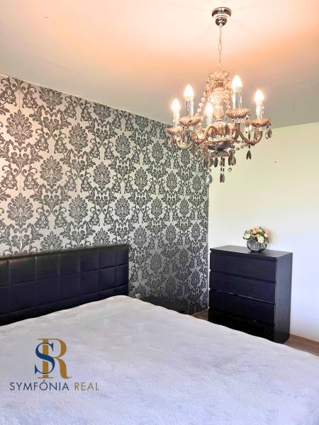 Ložnice s lustrem a tapetovou stěnou v rodinném domě. Podlaha s dřevěným dekorem.