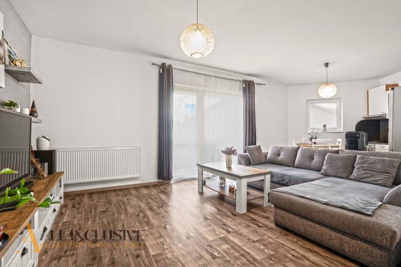 Obývací pokoj v 2-pokojovém bytě s podlahou s dřevěným dekorem a šedou sedačkou.