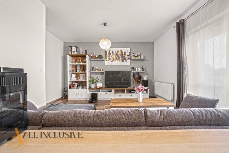 Obývací pokoj v 2-pokojovém bytě s podlahou s dřevěným dekorem a velkou sedačkou.