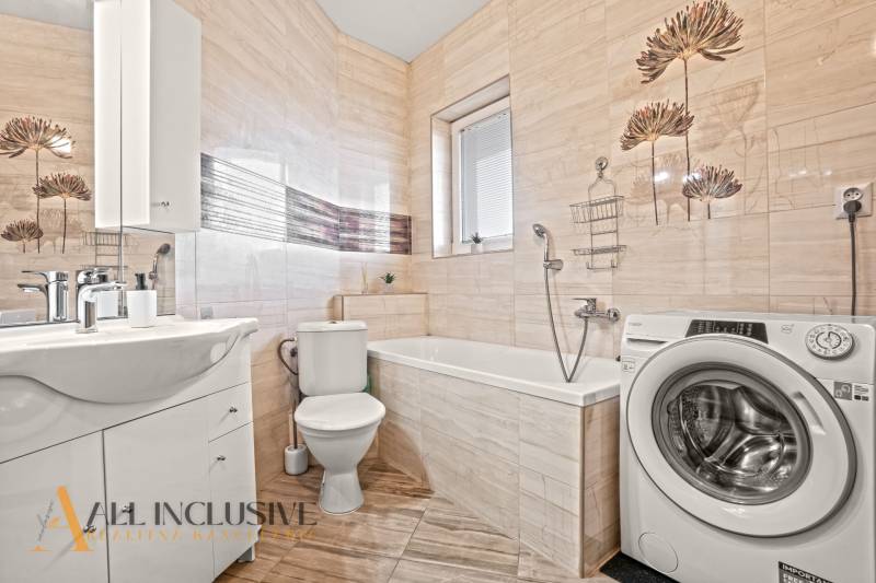 Koupelna v 2-pokojovém bytě s pračkou, vanou, umyvadlem a obloženými stěnami.