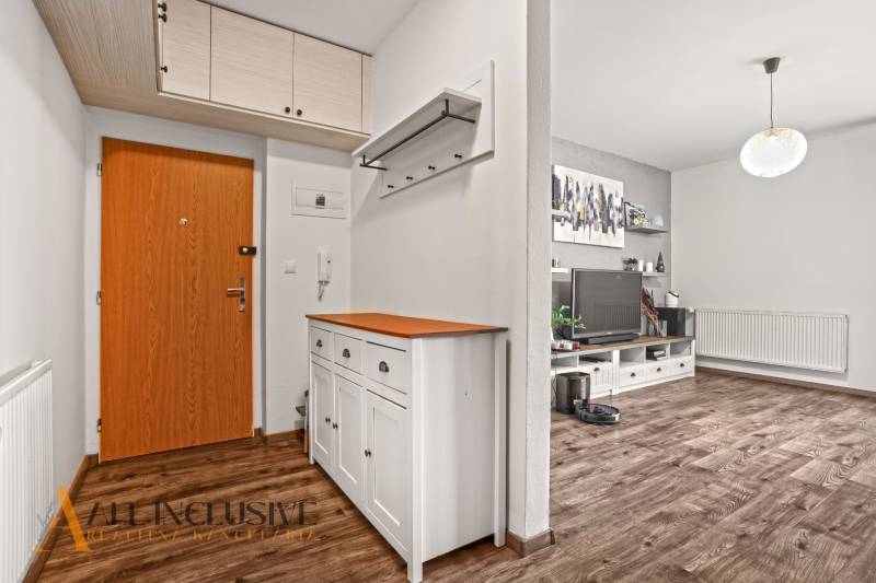 Vstupní chodba v 2-pokojovém bytě s podlahou s dřevěným dekorem a bílým nábytkem.