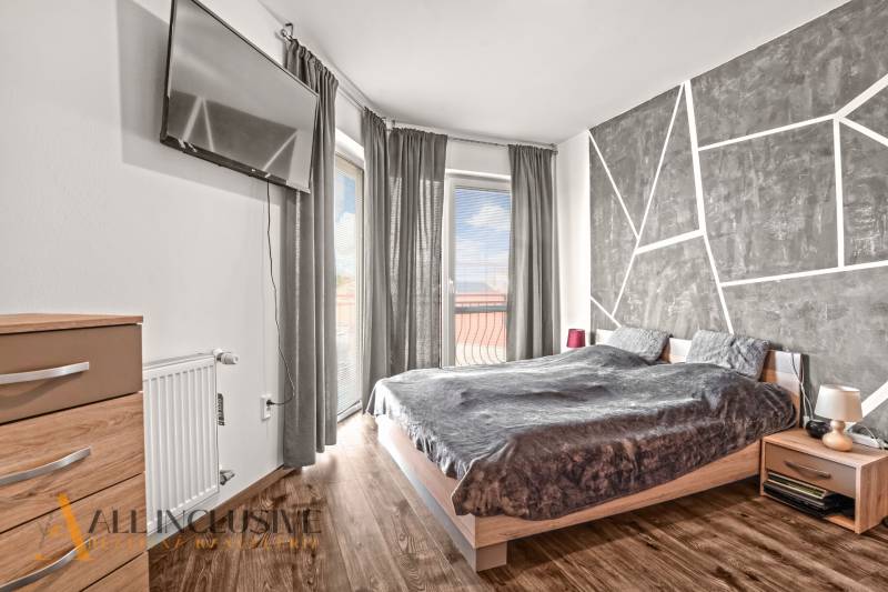 Ložnice v 2-pokojovém bytě s televizí, postelí a podlahou s dřevěným dekorem.