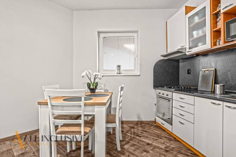 Kuchyně v 2pokojovém bytě s jídelním stolem a podlahou s dřevěným dekorem.