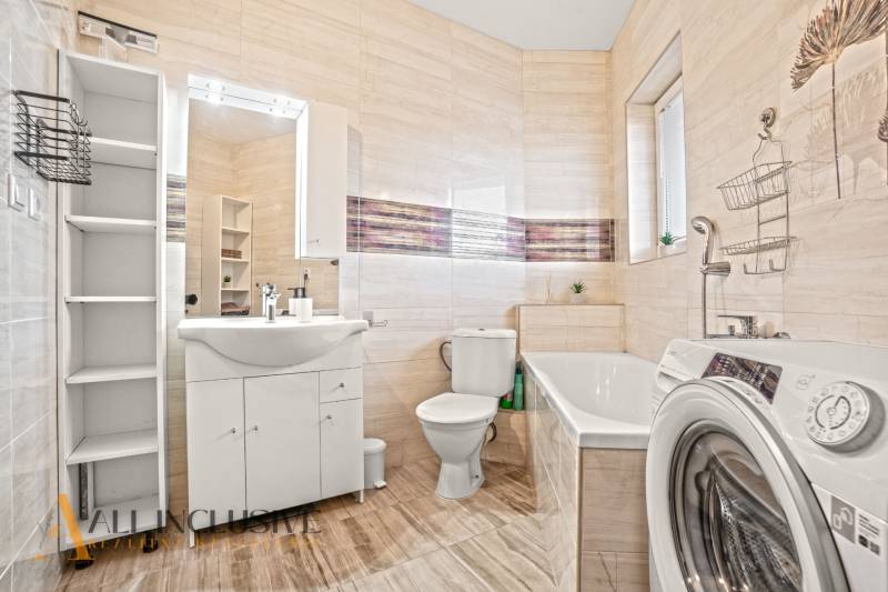 Koupelna se sprchou, vanou a pračkou v 2-pokojovém bytě, podlaha s dřevěným dekorem.