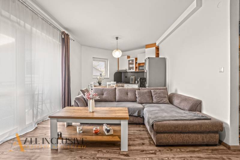 Obývací pokoj v 2-pokojovém bytě s pohovkou, kuchyňskou linkou a podlahou s dřevěným dekorem.