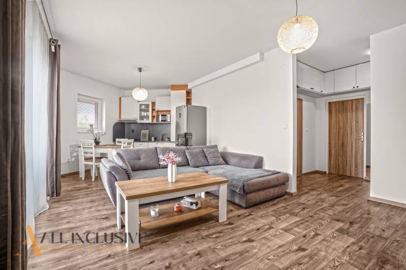 Obývací pokoj dvoupokojového bytu s pohovkou a podlahou s dřevěným dekorem.