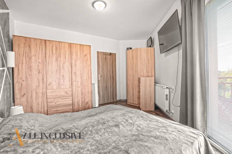 Ložnice v dvoupokojovém bytě s podlahou s dřevěným dekorem a šatními skříněmi.