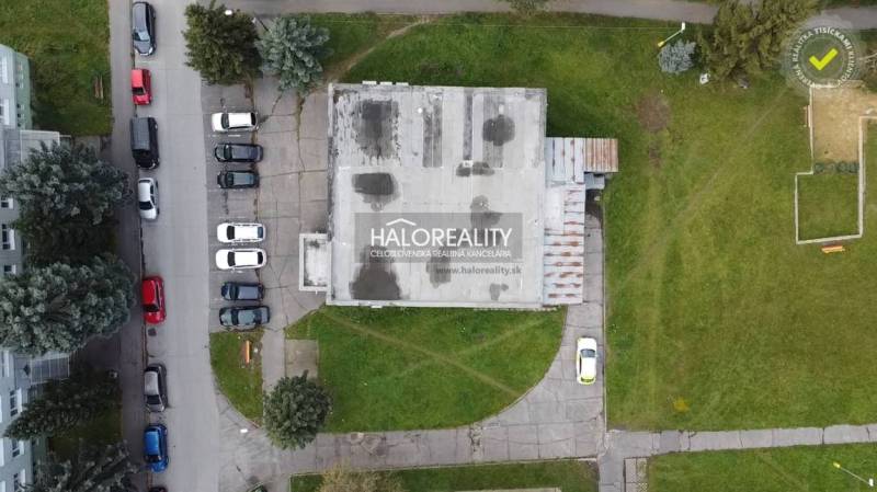 Pohled shora na obchodní prostory v Rimavské Sobotě, obklopené zelení a zaparkovanými auty.