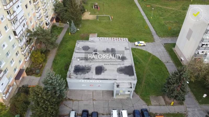 Obchodní prostory v Rimavské Sobotě s plochou střechou, obklopené zelení a bytovkami.