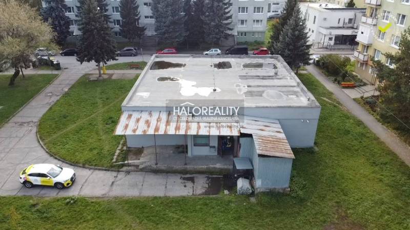 Pohled na obchodní prostory v Rimavské Sobotě s přilehlým parkem a betonovou střechou.