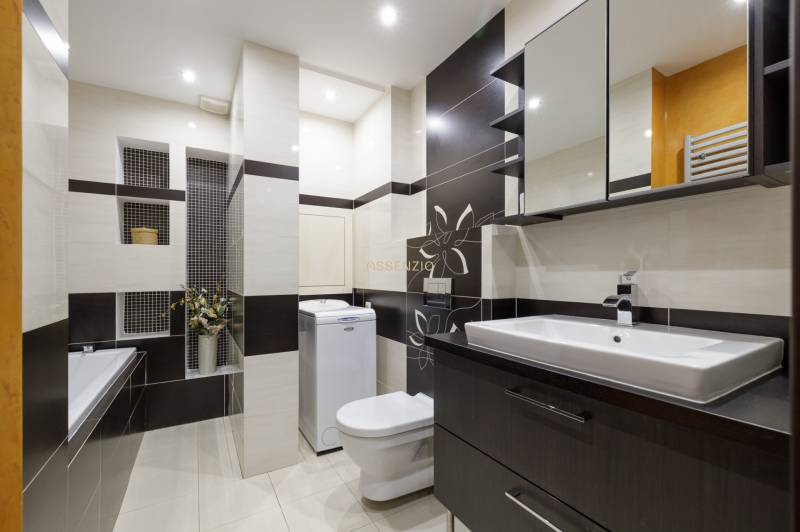 Koupelna v 2-pokojovém bytě se sprchovým koutem, pračkou a umyvadlem.