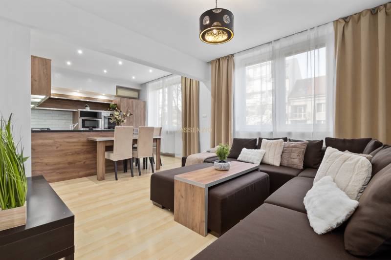 Obývací pokoj s podlahou s dřevěným dekorem v 2pokojovém bytě s rohovou sedačkou a kuchyní.