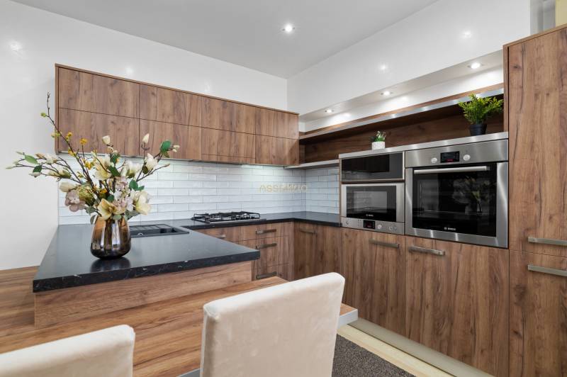 Kuchyně v 2-pokojovém bytě, dřevěný dekor, bílé obklady, vestavěné spotřebiče.