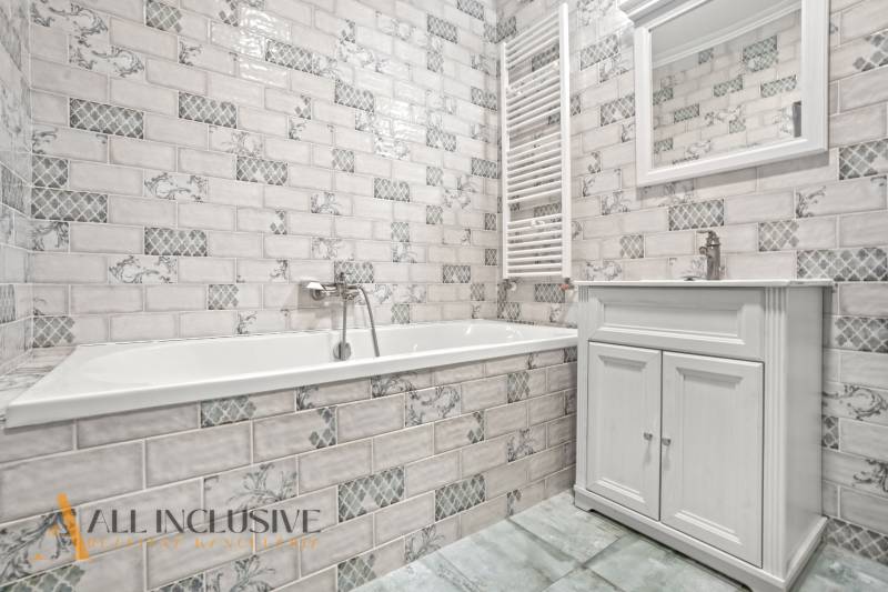 Koupelna ve vyhotovení 2pokojového bytu s bílými kachličkami a vanou.