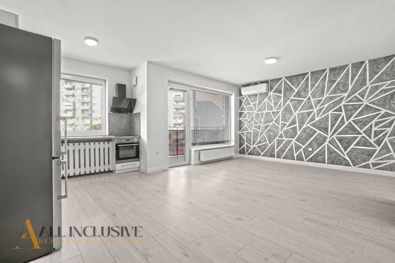 Kuchyně a obývací pokoj v 2-pokojovém bytě s podlahou s dřevěným dekorem a geometrickou stěnou.