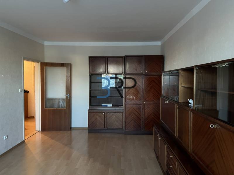 Obývací pokoj v 2pokojovém bytě s velkou dřevěnou obývací sestavou a podlahou s dřevěným dekorem.