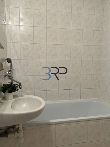 Koupelna s vanou a umyvadlem ve 2-pokojovém bytě, obložená kachličkami.