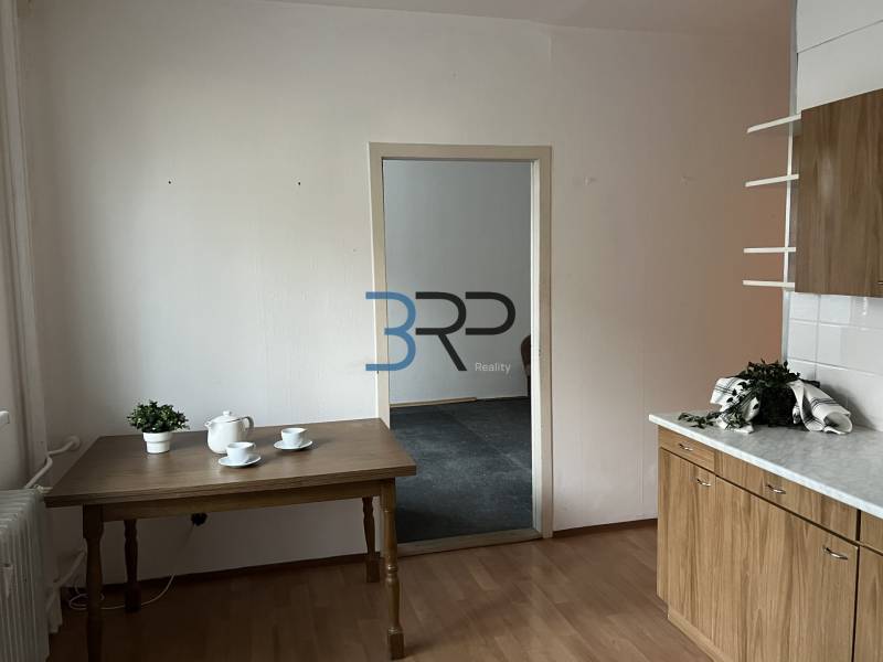 Kuchyně v 2-pokojovém bytě s podlahou v dřevěném dekoru, stolem a nádobím.