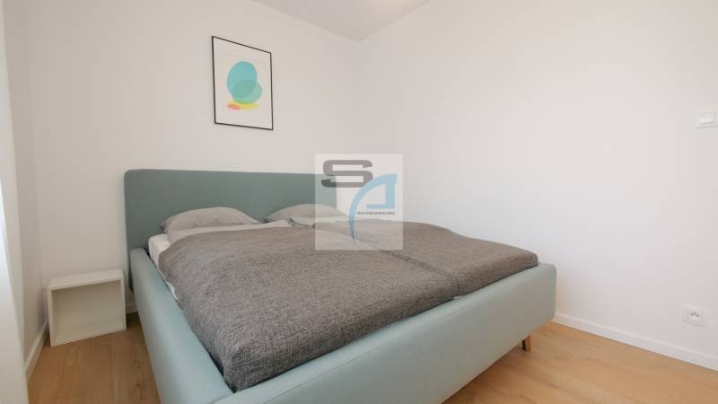 Ložnice s postelí a minimalistickou dekorací v 2pokojovém bytě, podlaha s dřevěným dekorem.