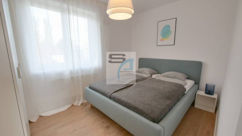 Ložnice s velkou postelí, záclonami a podlahou s dřevěným dekorem v 2-pokojovém bytě.