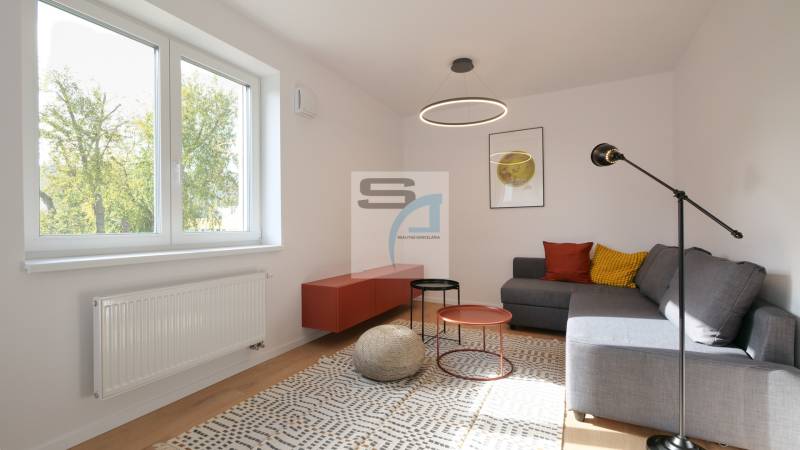 Obývací pokoj v dvoupokojovém bytě, sezení, barevné polštáře, konferenční stolky, koberec.