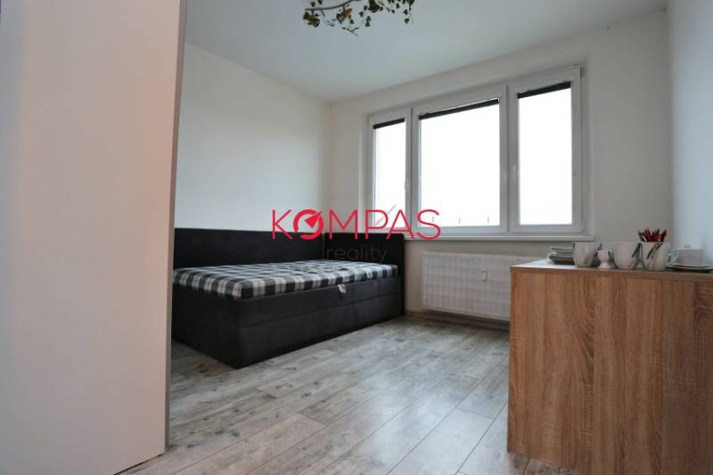 Pokoj v 3-pokojovém bytě, podlaha s dřevěným dekorem, gauč a komoda.