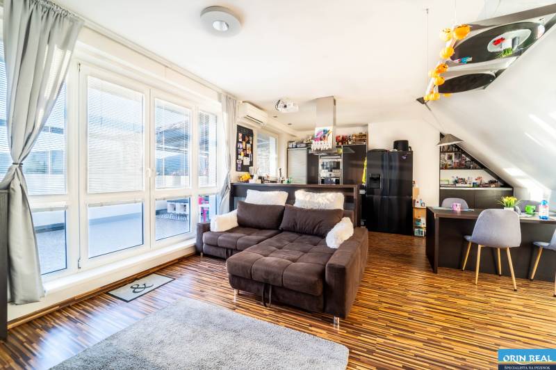 Obývací pokoj s pohodlnou sedačkou, podlahou s dřevěným dekorem a velkými okny v 2-pokojovém bytě.