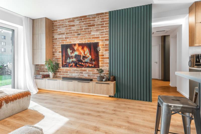 Obývací pokoj ve 3-pokojovém bytě s cihlovou stěnou, krbem a podlahou s dřevěným dekorem.