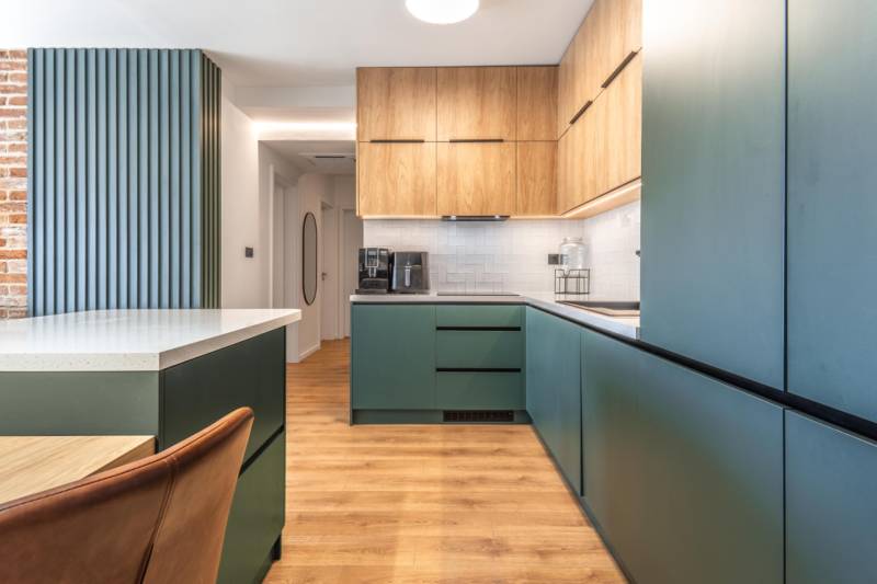 Kuchyně ve 3-pokojovém bytě s podlahou s dřevěným dekorem a zelenými skříňkami.