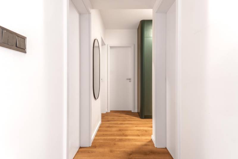 Úzký interiér s podlahou s dřevěným dekorem a jednoduchou bílou stěnou v 3-pokojovém bytě.