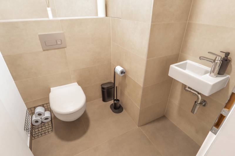 Toaleta se závěsnou mísou v 3-pokojovém bytě, béžové obklady, malé umyvadlo.