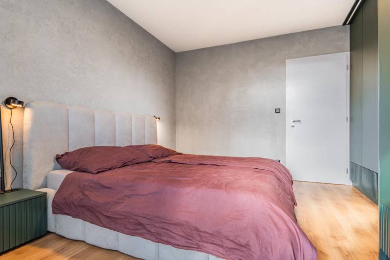 Ložnice s postelí ve 3pokojovém bytě, šedé stěny, podlaha s dřevěným dekorem.