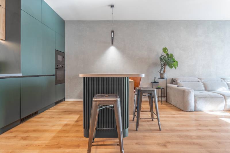 Kuchyně v 3-pokojovém bytě s ostrůvkem, kovovými židlemi a podlahou s dřevěným dekorem.