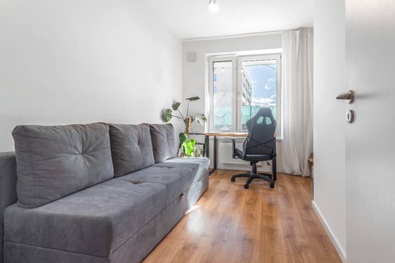 Světlý pokoj s pohovkou, kancelářskou židlí, stolem a podlahou s dřevěným dekorem.