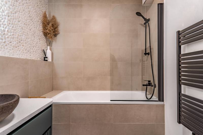 Koupelna s vanou, sprchovou zástěnou a dekorativními obklady v 3-pokojovém bytě.