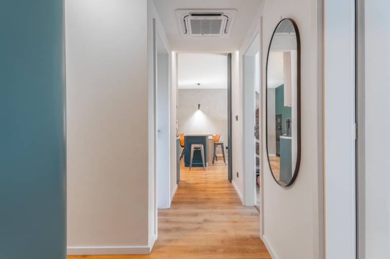 Interiér 3-pokojového bytu s podlahou s dřevěným dekorem a kulatým zrcadlem.