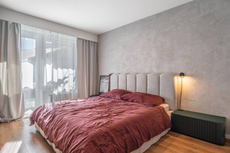 Ložnice v 3-pokojovém bytě s postelí, visícími závěsy a podlahou s dřevěným dekorem.