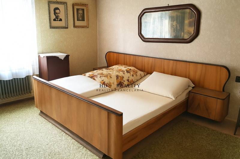 Ložnice s dřevěnou postelí, fotografiemi na stěně a zrcadlem v rodinném domě.