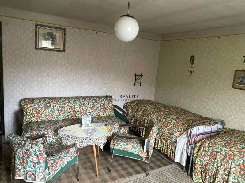 Pokoj v rodinném domě s retro nábytkem, vzorovanými potahy a kobercem.