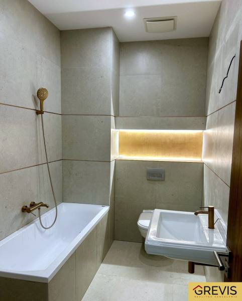 Koupelna s vanou, sprchovou hlavicí, WC a podsvícením ve 4pokojovém bytě.