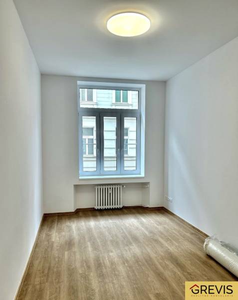 Pokoj se světlými stěnami a podlahou s dřevěným dekorem ve 4pokojovém bytě.