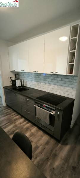 Kuchyně ve 3-pokojovém bytě s tmavými skříňkami a podlahou s dřevěným dekorem.