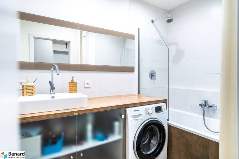 Koupelna s umyvadlem, pračkou a vanou v 3-pokojovém bytě, podlaha s dřevěným dekorem.