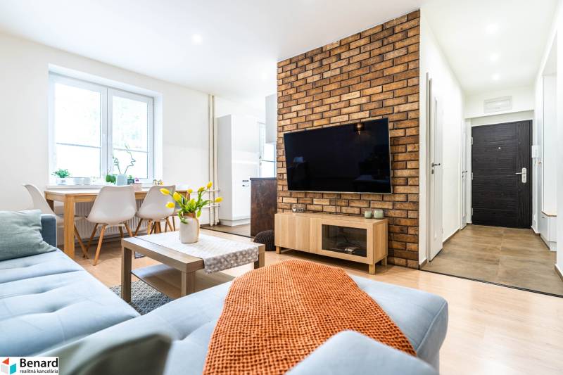 Obývací pokoj s pohovkou, stolem a TV, v 3-pokojovém bytě. Podlaha s dřevěným dekorem.