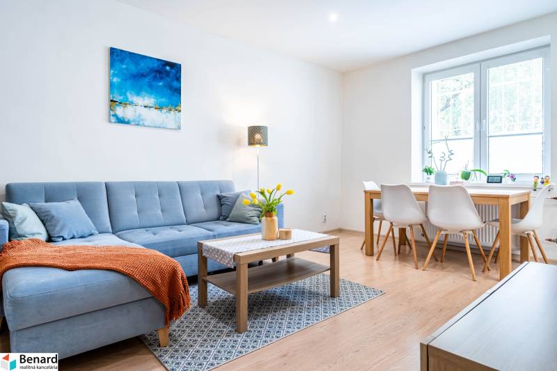 Obývací pokoj v 3-pokojovém bytě s pohovkou a jídelním stolem, podlaha s dřevěným dekorem.