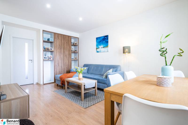 Obývací pokoj v 3-pokojovém bytě s modrou sedačkou a podlahou s dřevěným dekorem.